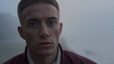 Deniz sahilinde kameraya poz veren üzgün adamın portresi. Yakından bakınca üzgün bir adam var. Erkek adam kameraya doğru dönüyor. Yavaş çekimde göz kırpan yakışıklı bir adam. Ciddi yüz ifadesi olan bir hippi.