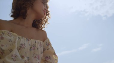 Güneşli deniz manzarasında beyaz spor ayakkabı giyen çekici kadın bacakları görünüyor. Hayalperest sakin kız, kumsalda tahta korkuluklarda oturuyor. Kıvırcık, güzel bayan güzel okyanusun tadını çıkar..