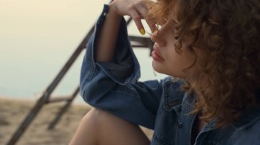 Düşünceli kadın sakin gri okyanusun yanında kumsalda oturup rahatlıyor. Çekici kıvırcık kız dizine sarı manikür yaptırmış. Hayalperest genç bayan kasvetli deniz manzarasının tadını tek başına çıkarıyor. Tatil kavramı.