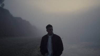 Deniz kıyısında yürüyen üzgün bir adam. Üzgün adam kendini yalnız hissediyor. Erkek model, gün doğumunda okyanus manzarası seyrediyor. Kameraya doğru gelen depresif bir adamın portresi. Sabahları dramatik sisli manzara 