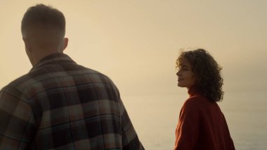 Gün doğumunda kumsalda sevgili bir çift. Deniz kıyısında yürüyen mutlu kadın ve adam. Romantik aşıklar el ele tutuşuyorlar. Gülümseyen kız okyanusta günbatımının tadını çıkarıyor. İlişki kavramı 