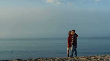 Deniz kıyısında duran sevecen bir çift. Sevgi dolu bir kadın sahilde bir erkeği yanaktan öpüyor. Okyanus ufkuna bakan şık arkadaşlar. Kız ve erkek romantik vakit geçiriyorlar. Duygular konsepti