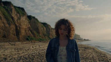 Okyanus sahilinde yürüyen hayalperest kız. Şık bir kadın gün doğumunda deniz manzarasını izliyor. Kadın model eller kıvırcık saçlara dokunuyor. Kıyıda duran genç bayan. Çekici kadın portresi Sakin deniz görünümlü 