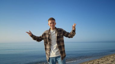 Pozitif adam güzel plaj güneşli bir günde rahatlarken kameraya merhaba diyor. Yakışıklı genç turist deniz manzarasının önünde video bloğu işletiyor. Gülümseyen adam doğayla ilgili blog yazarken konferans salonuyla konuşuyor..