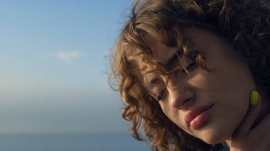 Kameraya poz veren şehvetli bir kız. Üzgün kadın yüzü. Kadın model el boyuna dokunuyor. Güzel bayan dışarıda düşünüyor. Hayalperest kadın portresi. Kıvırcık saçlı hippi kız denizde vakit geçiriyor.