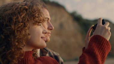 Kapalı çekim gülümseyen kadın ve erkek sahilde akıllı telefondan resim çekiyor. Mutlu çift tatilin tadını çıkarıyor. Hippiler cep telefonuyla fotoğraf çekiyor. Yüzünde olumlu ifade olan kız ve erkek portresi