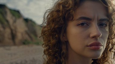 Sahilde güneşin doğuşunu seyreden düşünceli bir kadın. Hayalperest kız başını kameraya çeviriyor. Doğal makyajlı kadın modelin portresi. Dışarıdaki kameraya poz veren genç bayan. Kadın ciddi görünüyor.