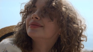 Kafasına hasır şapka takan neşeli genç kadın kumsala yakın duruyor. Sakin mavi okyanusun önündeki güzel kız yüzü görüntüsü. Gülümseyen çekici bayan turist güzel deniz kıyısında yaz tatilinin tadını çıkarıyor..