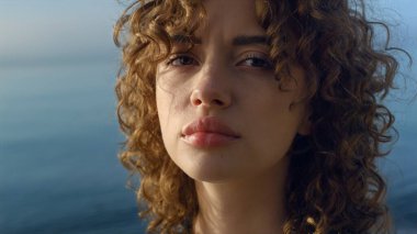 Kameraya bakan üzgün bir kız. Üzgün kadın yüzü portresi. Kadın model dışarıda poz veriyor. Sahilde yürüyen genç bayan. Deniz dalgaları kıyıya vuruyor. Okyanus arka planı. Üzüntü konsepti 