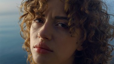Sahilde kameraya poz veren üzgün kadın. Gözünü kırpan depresif bir kız. Hüzünlü bir kadın. Sakin bayan kameraya bakıyor. Arka planda deniz olan kadın portresi. Hayal kırıklığı konsepti