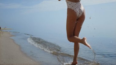 Bilinmeyen çıplak ayaklı kız su sıçratıyor okyanus dalgaları yaklaşıyor. Güzel ince bronzlaşmış bacaklar yaz günü ıslak deniz kumu üzerinde yürüyor. Mutlu, neşeli kadın deniz kıyısında rahatlarken sana iyi eğlenceler. Tatil kavramı.