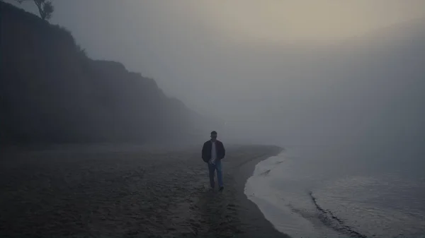 一个孤独的家伙在雾蒙蒙的日出中走在海滩上 漫无目的的人在雾中探索自然 男性嬉皮士在海洋度假 落基山脉坐落在海滨 忧郁的气氛 — 图库照片