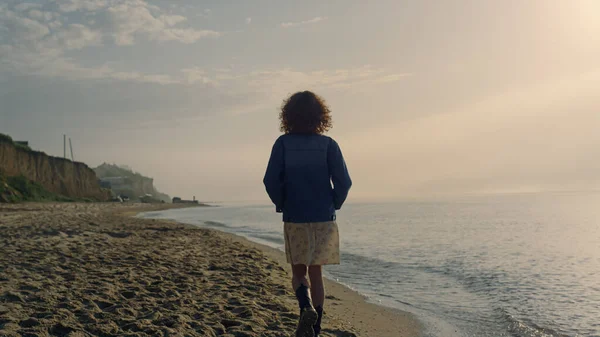 在沙滩上散步的休闲妇女的背景 一个在日出时探索大海海岸的时髦女孩 女嬉皮士手插在夹克口袋里 女士享受大自然 日落时的海景 — 图库照片