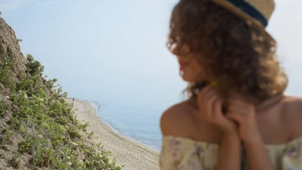 Portrait of dreamy gorgeous girl watching sunny landscape beautiful seashore. Attractive young lady relax on sand beach wearing straw hat close up. Carefree happy woman relax on nature summer day.
