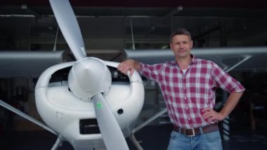 Pilot uçak, beyaz uçak gövdesine yaslanmış bir hangar gibi duruyor. Havalimanında küçük bir uçağın bakımını yaptıktan sonra tek başına rahatlayan mutlu profesyonel havacı görüntüsü..