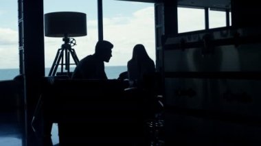 İş adamları karanlık ofis işyerinden bahsediyorlar. İş ortakları, karanlık deniz manzaralı konferans salonunun fikirlerini paylaşıyorlar. Bilinmeyen bir çift panoramik pencerelerde flört ediyor. 