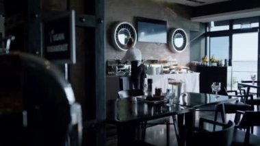 Elegant waitress preparing open breakfast buffet in panoramic cafe bar hall. Cozy dark hotel restaurant dining area view. Lunch served tables in stylish cafeteria interior. Event catering concept.
