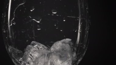 Soğuk bloklar cam kırıkları yakın plan. Buz küpleri içine şeffaf şarap kadehlerini süper yavaş çekimde atıyor. İçecek makro siyah arka plan tazeleniyor. İçki ve kokteyl konsepti hazırlanıyor.