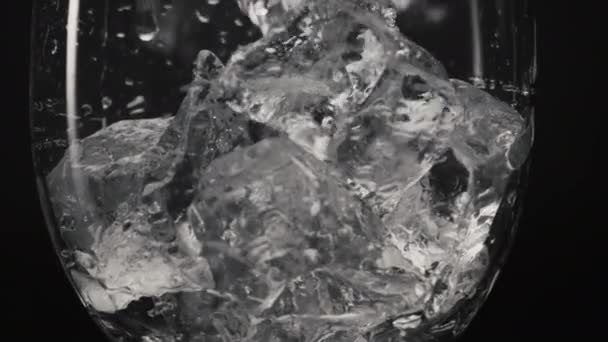 冰块滑落玻璃特写慢动作 被冻结的碎片倒入透明的滴下的玻璃杯中 冷饮和鸡尾酒宏观黑色背景 口渴者概念 — 图库视频影像