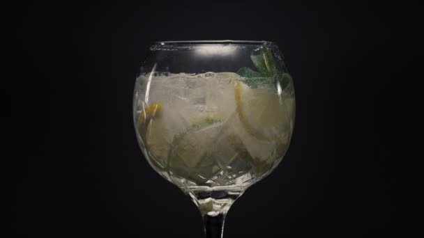 固定レモンアイスミントの泡カクテルを閉じます ワイングラスの超スローモーションで滴と氷のキューブとビタミン水を輝く マクロビューブラックサーフェスの背景 夏の新鮮な冷たい飲み物のコンセプト — ストック動画
