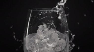 Soğuk buz küpleri yakın plan cam içerler. Şeffaf şarap kadehinden akan temiz su yavaş çekim tespiti yapıyor. Köpüklü su siyah arka plan dökülüyor. Taze soda kokteyli.