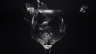 Buzlu limonlar boş şarap kadehlerini birbirine yaklaştırır. Donmuş bloklar nane ve limonlar şeffaf cama süper yavaş çekimde fırlatılıyor. Makro siyah arkaplan kuruluyor. İçecek konseptini tazelemek