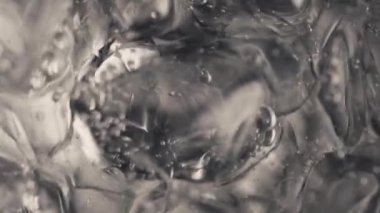 Buz küpleri köpüren su yavaş çekimde dönüyor. Hava damlaları buzla kaplı, soda bardağı köpüklü suyla. Kabarcıklar yüzey makro üst görünümünde patladı. Saf meşrubat konseptini tazeliyorum.