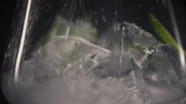 Soğuk nane likörü şarap kadehini yakın plan doldurur. Köpüklü soda jeti, bardakları otlarla dolduran makro manzaralı siyah arka plan. Mojito ferahlatıcı lezzetli karbonatlı kokteyl konsepti