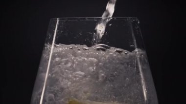 Limonlu naneli su yakın plan içki bardağı. Buzlu soda içeceği makrodaki şarap kadehini dolduruyor. Köpürmüş limonata sıvı siyah arka plan görüntüsü. Cin tonik kokteyli konsepti hazırlanıyor