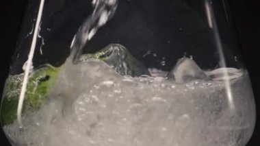 Soğuk sıvı naneli şarap kadehi yakın plan. Karbonatlı maden suyu jeti, bardağı nane şekerli makro manzaralı siyah zemin ile dolduruyor. Ev yapımı antioksidan kokteyl konsepti