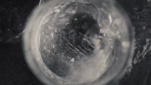 氷のキューブの落下ミネラルウォーターのガラスを閉じ込めた 透明なガラスの中で固まったソーダ冷たい飲み物 スプラッシュはスローモーションで異なる方向に散布されます カクテルプロセスのコンセプトを作る — ストック動画