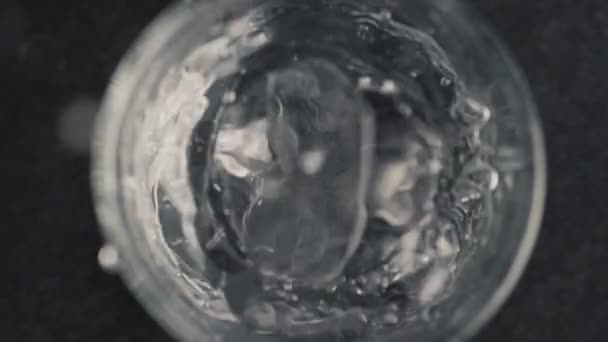 碎冰块掉落矿泉水杯 冰块在清凉的饮料中旋转在透明的杯子中 超慢速运动 俯瞰黑色背景 准备饮料和鸡尾酒概念 — 图库视频影像