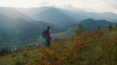 Active millennial travel mountains nature. Young woman trekking on landscape summer morning. Sporty explore walk on outdoors vacation. Excited tourist reach peak on green hill. Youth adventure concept