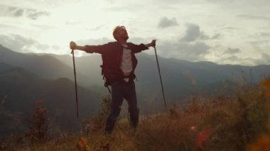 Free backpacker enjoy mountains landscape. Happy tourist relax at morning nature. Silhouette of emotional guy look picturesque landscape. Excited traveler hiking reach peak. Travel lifestyle concept.