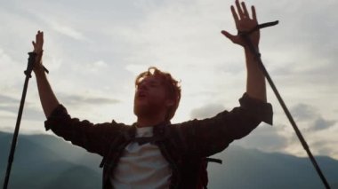 Closeup excited backpacker celebrate victory in nature. Active young traveler reach mountains peak. Emotional guy raise hands on tourism trip. Successful tourist scream outside. Happiness concept.