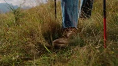 Closeup hiking boots legs trekking in mountains. Sporty tourist walk going green hill. Active man feet travel outside in autumn nature. Unrecognizable guy using hike poles equipment. Leisure concept.