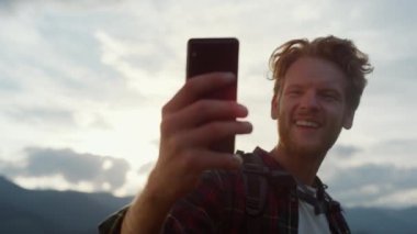 Closeup excited blogger take selfie on mobile phone outdoors. Hipster celebrate reach peak on mountains. Emotional traveling guy express happiness on digital smartphone. Technology leisure concept.