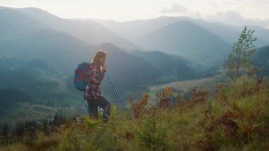 Excited woman trekking landscape outdoors. Active girl enjoy forest mountains holiday. Smiling backpacker hiking in summer morning. Joyful explorer going tourism adventure. Youth lifestyle concept.