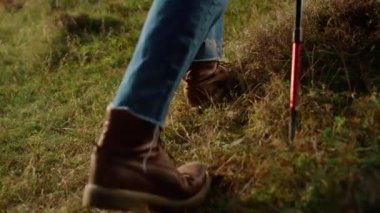 Closeup man legs climb mountains grass slope. Unknown tourist hiking on green hill outside. Traveler feet wear trekking boots on expedition trail. Sporty hiker using travel equipment. Leisure concept