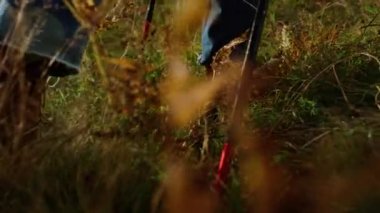 Closeup hiker legs walk mountains hill. Active traveler feet wear hiking boots on grass. Unrecognizable man climb green slope using trekking poles equipment. Journey activity sport recreation concept.