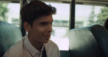 Gülümseyen Hintli okul çocuğu okul otobüsünde konuşuyor. Yaklaş. Mutlu, çok kültürlü bir öğrenci taşıma aracının portresi. Neşeli esmer çocuk sınıf arkadaşıyla sohbet ediyor. Rahat genç gezintiden zevk alıyor.