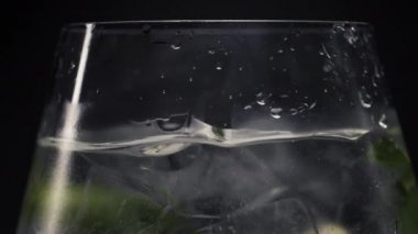 Limon, naneli buzlu, köpüklü kokteyl yakın plan. Meyve parçası şarap kadehi fırlatır ve dalgaları çok yavaş hareket ettirir. Cin tonik içeriği makro görünüm siyah arka plan. Yaz içecekleri konsepti