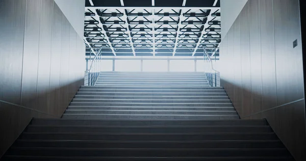 Empty bright school staircase interior. Light shining through glass window. Long clean stairway corridor heading towards lobby in large building. Lamps on ceiling. Modern construction concept.