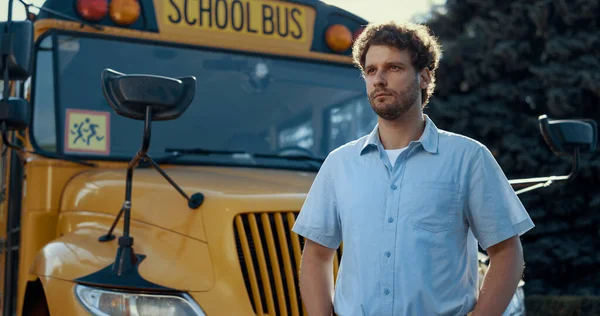 Portrait of schoolbus driver standing at yellow vehicle alone looking camera. Serious professional chauffeur wearing uniform posing at classic school shuttle. Pensive bearded man. Profession concept.