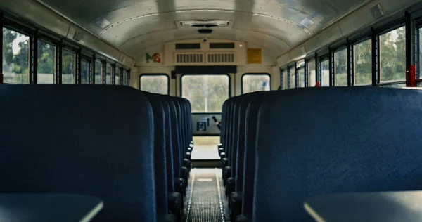 Empty school bus saloon with comfortable blue seats close up. View of aisle inside modern public transport. Students vehicle with vacant placements waiting boarding. Schoolbus staying parking.