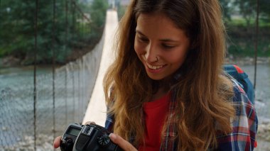 Gülümseyen kız güzel doğayı fotoğraflamaktan hoşlanır. Heyecanlı bir kadının portresi, dağ manzarasında dijital kamera fotoğraflarını kontrol ediyor. Turist fotoğrafçı resimlere bakıyor. Hobi konsepti.