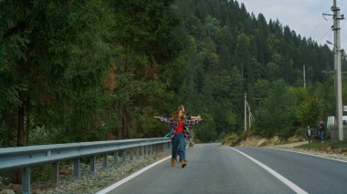 Dağlarda yol kenarında yürüyüş yapan mutlu yürüyüşçüler. İki arkadaş güzel doğa manzarası için el kaldırıyor. Tatilde otoyola atlayan heyecanlı çift. Seyahat eğlence konsepti.