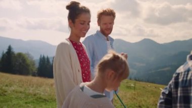 Happy parents with two children resting on summer mountains. Cheerful family spending vacation on beautiful green hill. Redhair man looking at pretty woman with kids enjoying sunny day close up. 