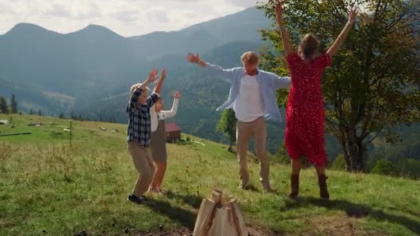 Смеющаяся Семья Прыгает Поднимая Руки Зеленый Холм Солнечный День Играющие — стоковое видео