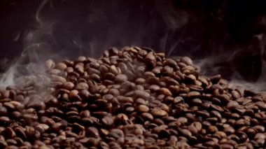 Steam rising over hot coffee beans heap close up. Roasting process caffeine seeds in slow motion. Fragrant coffee grains on pile with great aroma. Perfect ingredient for preparing energetic beverage.